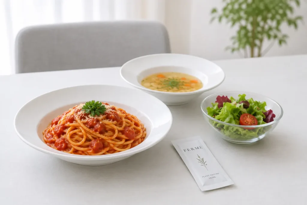 白いテーブルにトマトソースのパスタ、野菜スープ、ミニトマト入りのサラダが並び、手前にFERMÉの個包装スティックが置かれています。個包装に「FERMÉ PLANT ENZYME DRINK」と書かれています。